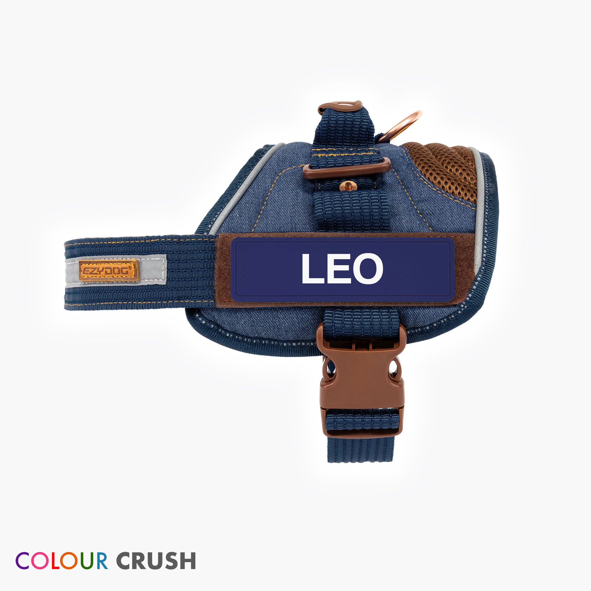 A blue denim dog harness with the name 'LEO' printed on a label, featuring a stainless steel D-ring, reflective trim, and a moulded grab handle.