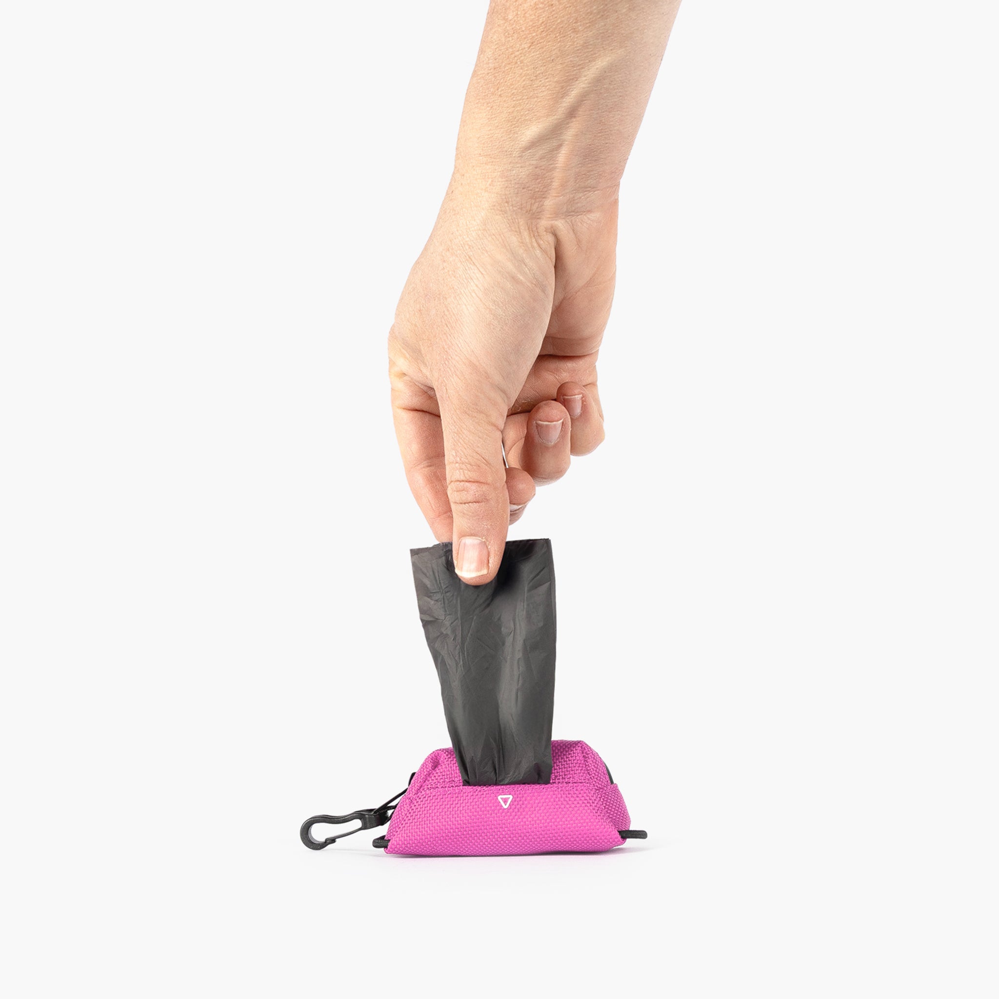 Hand holding a black trash bag over a pink Essential Poop Bag Holder with a carabiner clip on a white background