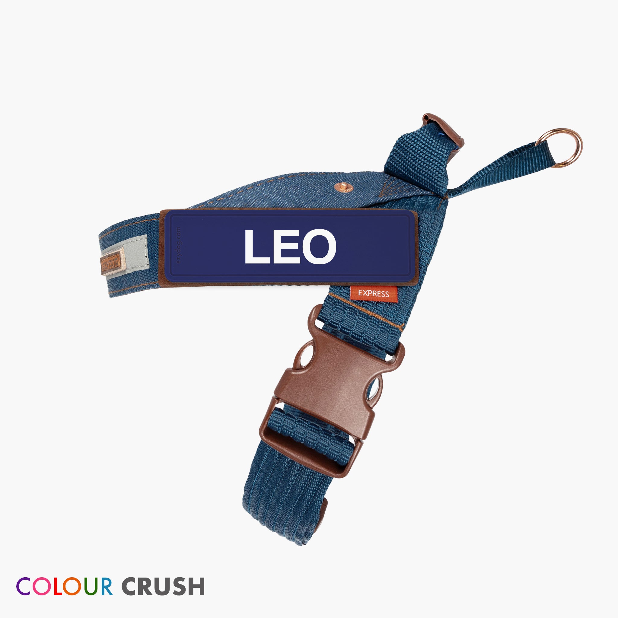 A blue denim dog harness with the name 'Leo' printed on the label, featuring a stainless steel D-ring and a moulded grab handle.